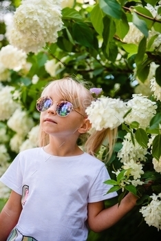 Beautiful little girl in stylish sunglasses in blooming flowers.